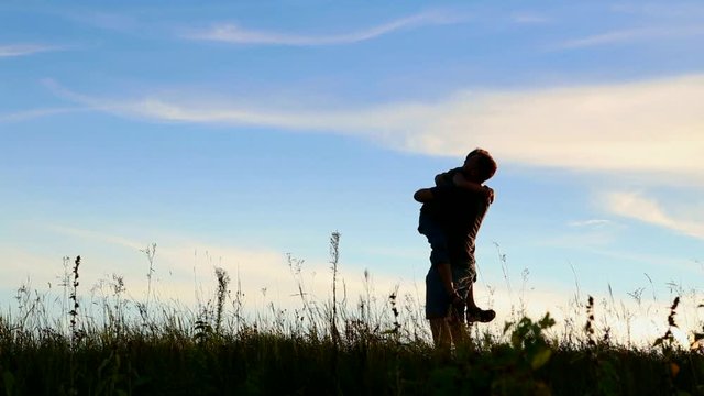 Happy child rushes into hands of father. Family hugs over sunset blue sky background. Silhouettes of anonymous boy and man outside in summer or autumn landscape. Full hd video portrait of dad and son.