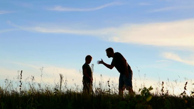 Angry parent and his child over sunset sky background. Anonymous emotional father talking and screaming at little guilty son outside. Feelings and emotions concept. Real time full hd video footage.