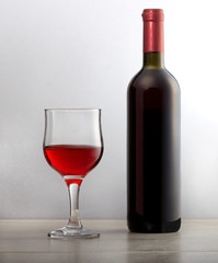Натуральное красное вино в стеклянном бокале и бутылка вина на столе из дерева.