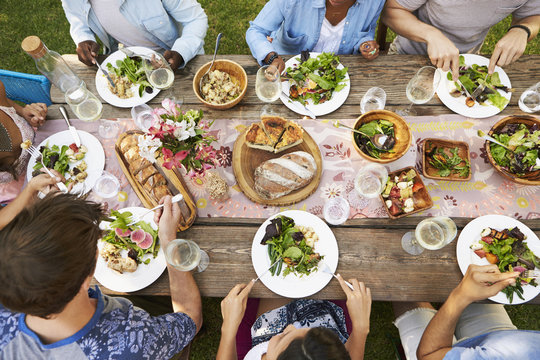 Overhead view of friends enjoying lunch and wine on wooden table outdoors