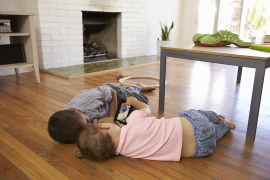 Siblings using mobile phone while lying on wooden floor at home
