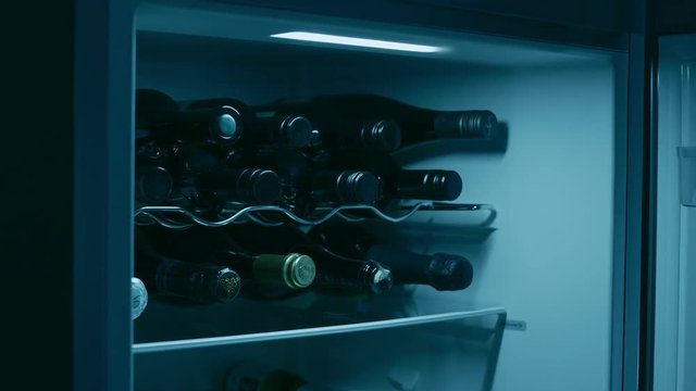 Wine bottles in a rack in the refrigerator. The refrigerator door opens, a wine bottle is removed