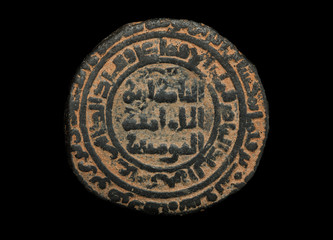 Ancient round islamic copper coin with arabic letters isolated on black