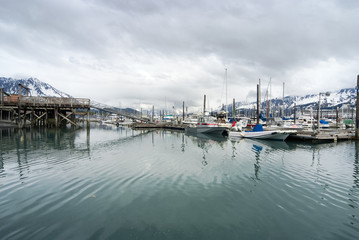 Fototapeta premium View of fishing boats moored at the port of Seward and snow covered mountains, Alaska