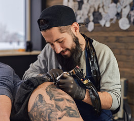 Tattoo master in black gloves, tattoo on the skin of black ink tattoo of his client in the salon.