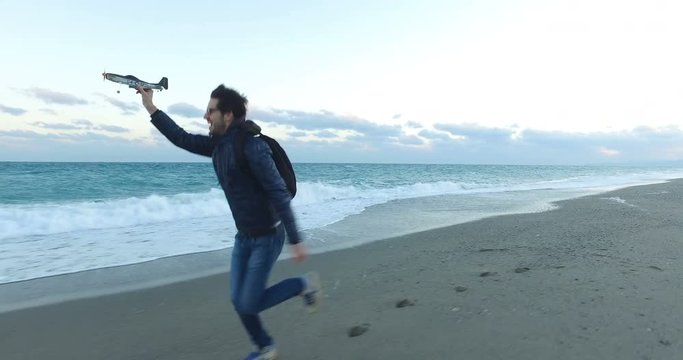 Ragazzo che sta correndo con un aereo giocattolo in riva al mare sulla spiaggia.