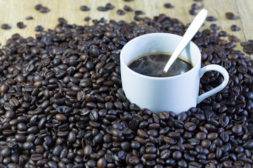 Cup of coffee in pile of seeds of coffee on brown plate / Blurred and Select focus image