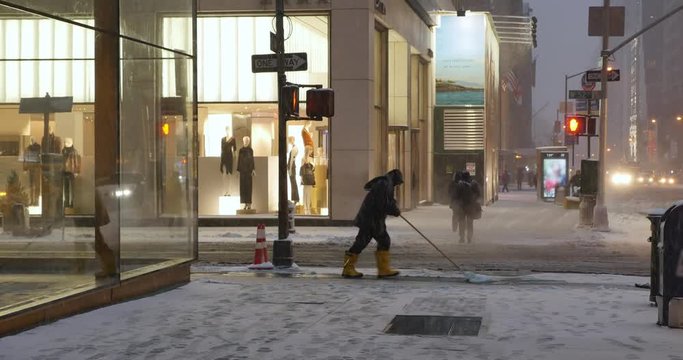 NEW YORK - Circa December, 2016 - A man shovels snow from the sidewalks outside upscale 5th Avenue businesses and storefronts.  	
