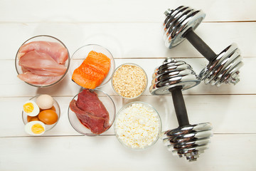 Protein diet, fish, cheese, eggs, meat, chicken and dumbbells on a white wooden background