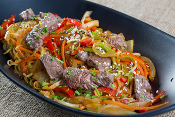 Close up of beef cuts, vegetables and spaghetti on a black plate