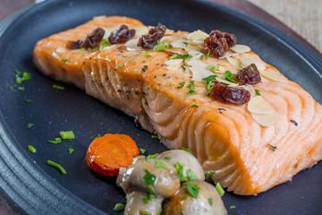close up with grilled salmon and boiled mushrooms on a black pla
