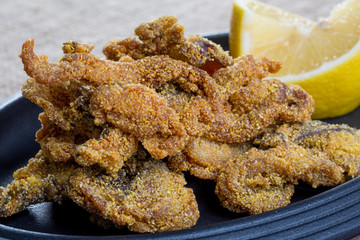 Close up of fresh fried fish parts with lemons on a black plate