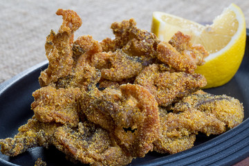 Close up of fresh fried fish parts with lemons on a black plate