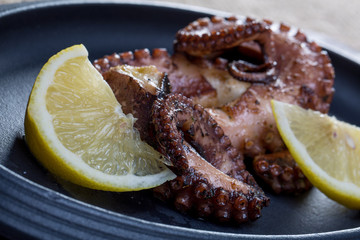 Close up squid tentacles with lemon on black plate