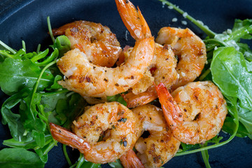 close up with fresh fried shirmps with arugula on a black plate