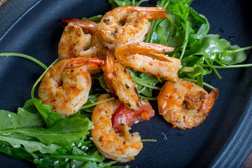 close up with fresh fried shirmps with arugula on a black plate