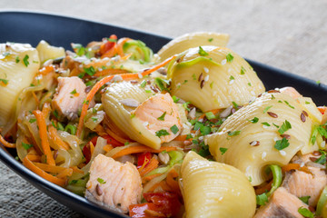 close up of salmon with large pasta and vegetables in a black pl