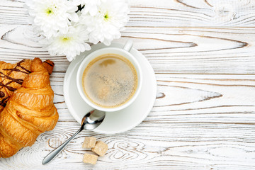 two fresh croissants and coffee, flowers on wooden background