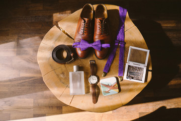 Man's wedding fashion. Groom's bow tie, watch, suspenders, belt and perfume lie on vintage wooden table. Modern outfit, items top view, flat lay.
