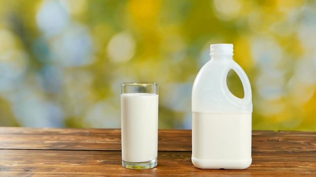 Bottle of milk and glass with milk in the garden on wooden table