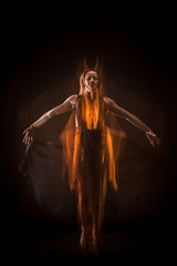 Young beautiful dancer in beige dress dancing on black background