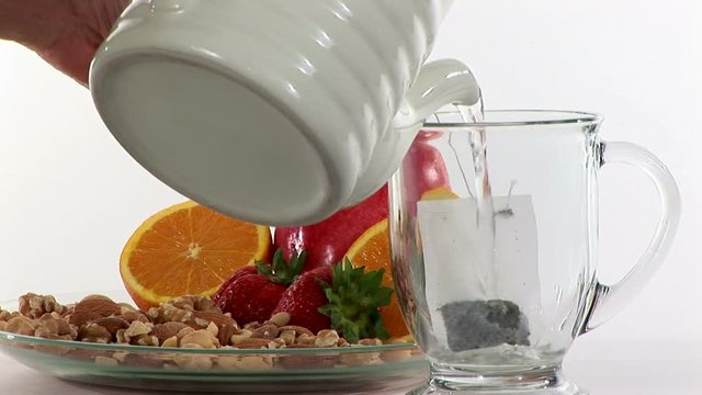 Brewing a cup of green tea with nuts and fruits placed near by.