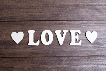 Word love with white letters between two hearts on brown wood.