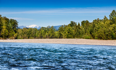 Swift current of the Skykomish River in Monroe, Washington with a sunny backdrop of the Cascades to...