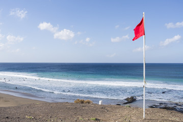 Red beach flag on a pole signaling alert pictured against deep b