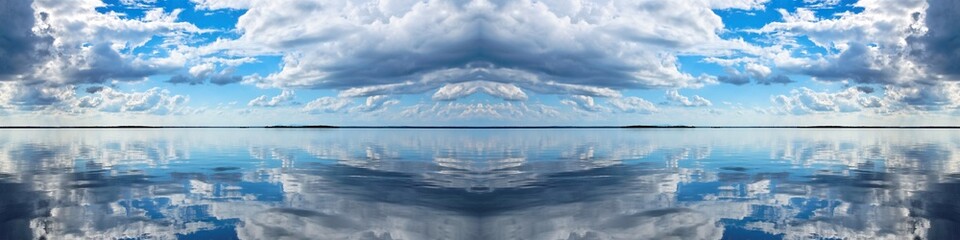 Cloudscape Panorama. Spectacular blue and white panoramic cloudscape with clear water reflections. Photograph was shot at sea from the deck of a boat looking toward land.
