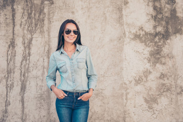 Portrait of trendy young woman in glasses standing near stone wa