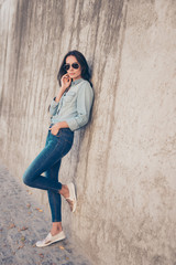 Young woman in glasses wearing jeans clothes standing near  ston