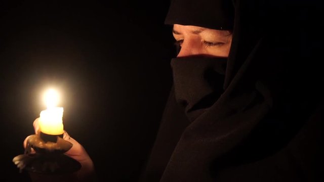 Portrait of person in burqa holding burning candle in dark room