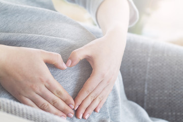 Pregnant woman holding her hands on her swollen belly shaping a