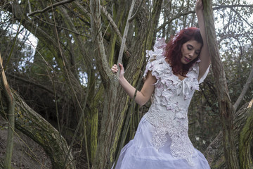 Fototapeta premium Beautiful red-haired woman in a forest with a cage containing co