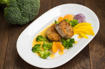 Delicious fillets fish roasted in the frying pan. Posted with tangerine sauce, pepper and slices of boiled broccoli al dente. Wooden background. Top view. Close-up