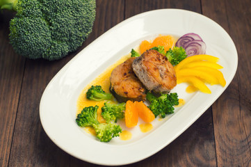 Delicious fillets fish roasted in the frying pan. Posted with tangerine sauce, pepper and slices of boiled broccoli al dente. Wooden background. Top view. Close-up
