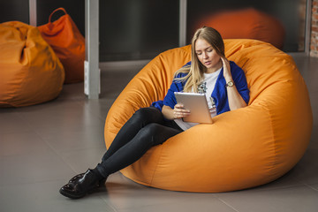 Armchair traditional bean bag for fun and relaxation  orange color. Young woman  using tablet...
