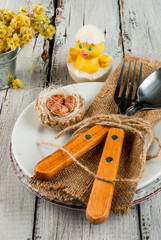 Spring Easter wooden table setting with plate, decorative nest with egg, flowers, cutlery and napkin. Copy space