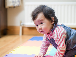 Naklejka premium adorable baby girl crawling on paly mat at home