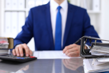 Binders with papers are waiting to be processed with businessman back in blur. Accounting planning...