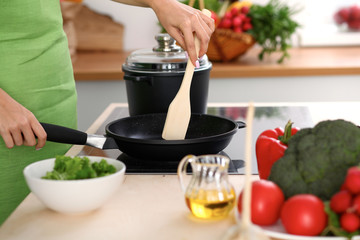 Young woman is cooking by the stove in the kitchen, close up.