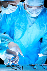 Medical team performing operation. Group of surgeon at work in operating theatre toned in blue.