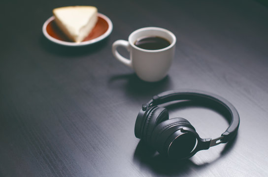 Headphones on a dark background. Music accessories. Bluetooth headphones without cable. Cake and coffee