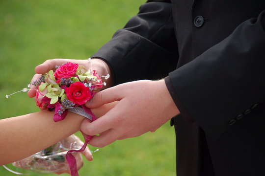 Young man slides wrist corsage onto prom date