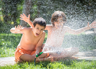 Cute little boys on summer meadow splashing water having fun and