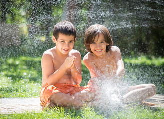 Cute little boys on summer meadow splashing water having fun and