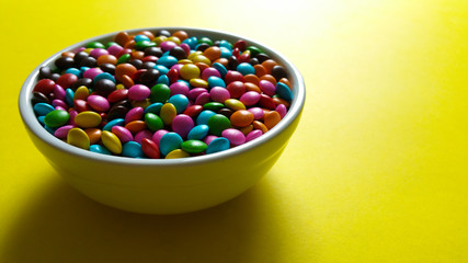 Colorful candy confetti in white pot with yellow background