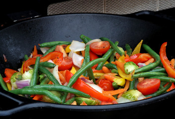 Close up photo of wok stir fry covered by smoke in a grill. A wok with assorted vegetables such as carrots, beans, red and yellow pepper, onion and brussels sprouts for vegetarian healthy eating.
