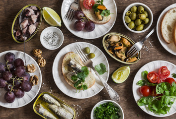 Snacks table - canned sardines, mussels, octopus, grape, olives, tomato on wooden table, top view. Flat lay
